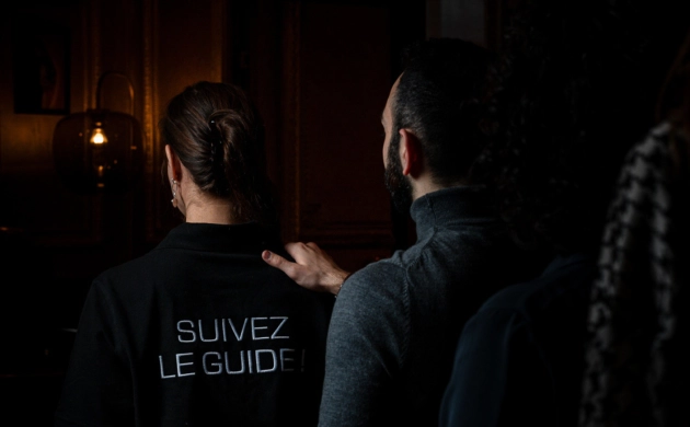Des convives suivent un guide dans l’obscurité, main sur l’épaule, pour vivre une expérience immersive autour d’un dîner chez Dans le Noir ? Genève.